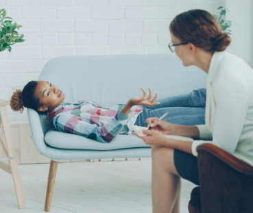 A young girl talks to a therapist on a couch.